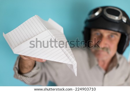 Senior funny man as a pilot with hat and glasses using paper plane