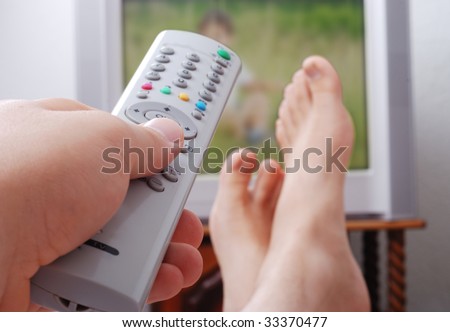 Remote control used by adult man in his hand and the legs are on the table