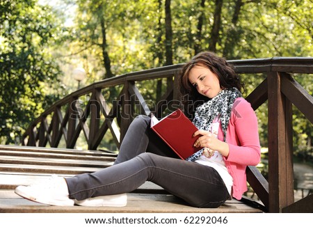 Young beautiful girl student sitting on wooden bridge in nature and reading a book