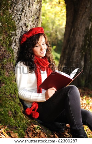 Beauty gorgeous autumn girl sitting in nature beside the tree and reading the book and studing