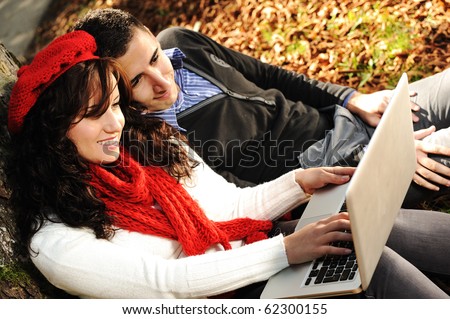 Young couple, male and female sitting in park and studying and working together with notebook , fall period
