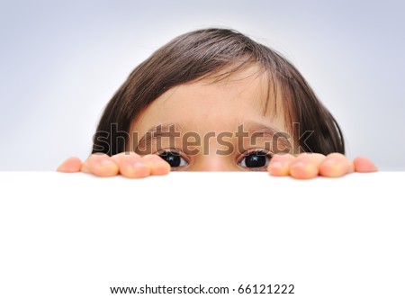 Child holding an empty sign over a white background, hiding behind, copy space