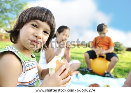 Happy group of children outdoor on meadow: eating and playing together