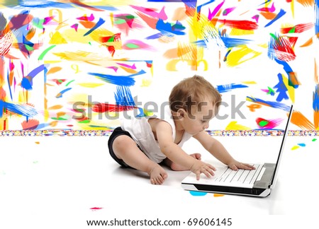 Little baby boy is sitting on floor with his laptop, isolated over white wall, in messy painted room with many colors around