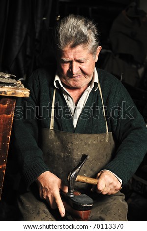 Elderly man, shoemaker repairing old shoe in his workshop
