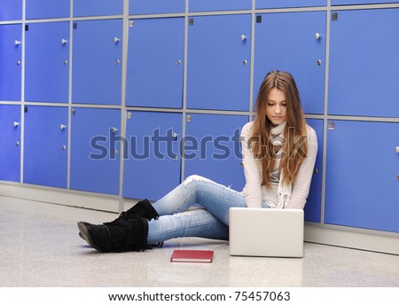 Beautiful female student sitting on ground at university with laptop