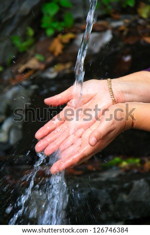 Transparent flow of a mountain stream caressing hand woman.