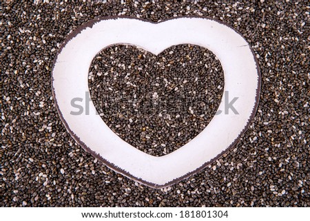 Background of organic chia seeds with white wood heart shaped frame inside.