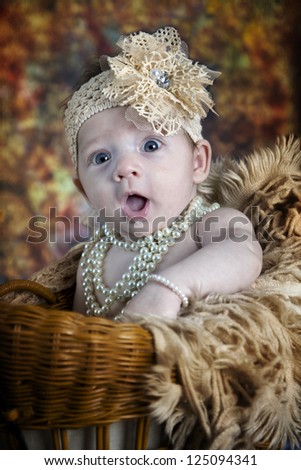 Beautiful little blue-eyed baby girl with bows,  pearls and fun expression