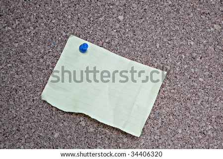 Textured cork bulletin board with torn piece of lined notebook paper attached with blue push pin. Ready for your text.