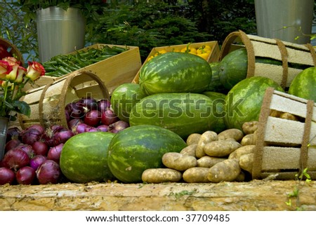Market display of beautiful roses, purple onions, watermelons; green and yellow peppers, and potatoes with baskets and boxes.
