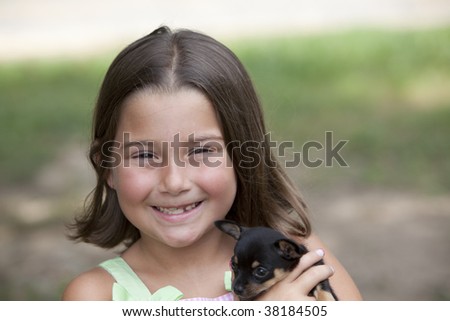 Beautiful little brown eyed brunette girl with missing teeth holding a tiny chihuahua outdoors with natural green background