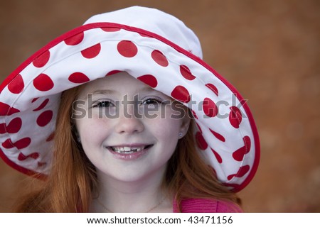 Beautiful little redheaded girl outdoors in red and white hat with missing teeth