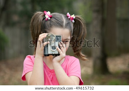 Cute little eight year old girl with pigtails and an old camera; flash and bulb outdoors