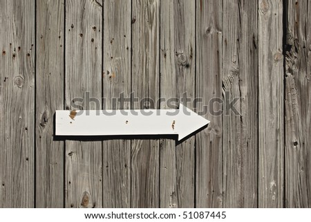 Old weathered wall or fence with white painted arrow sign and rusted nail heads showing