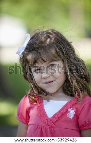 Beautiful little 3 year old girl brunette with white bow in her hair and pink and white shirt standing outdoors in wooded area