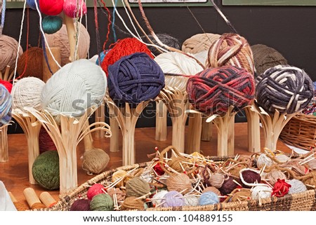 colored balls of wool on wooden rustic supports and in a basket with needles - a variety of yarns for knitting