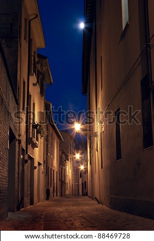 narrow dark alley in the old town -street at night in the Italian city lit by streetlights and the moon - romantic cityscape in Emilia Romagna, Italy
