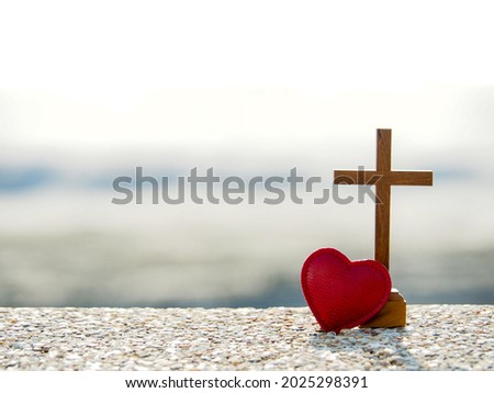 Photo of Red heart with wooden Christian cross on gravel floor in morning light, beach sea as background. Jesus love you. Faith hope believe in God. Believe in salvation. Christianity background concept.