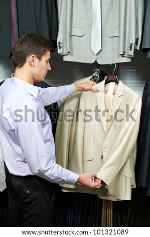 Young man choosing suit jacket during apparel shopping at clothing store