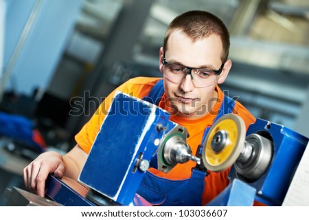 manufacture worker in uniform and protective glasses working on sharpening machine tool