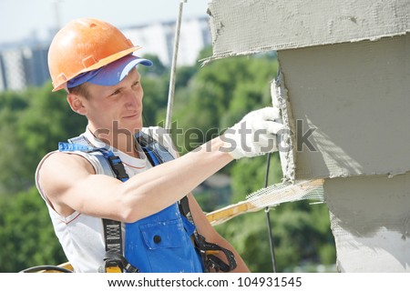 builder worker plastering facade of high-rise building with putty knife