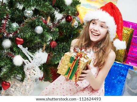 happy smiling little girl in Christmas pink hat with gifts near decorated new year tree