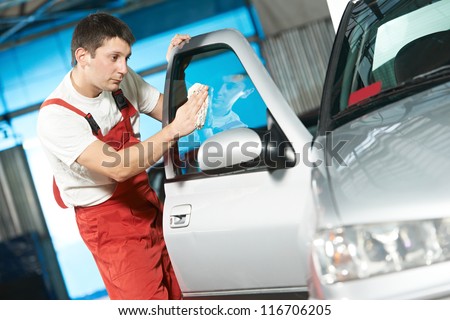 One young service mechanic cleaning automobile car door glass at auto repair shop