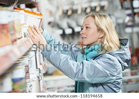 Young woman choosing color paint during hardware shopping in home improvement store supermarket