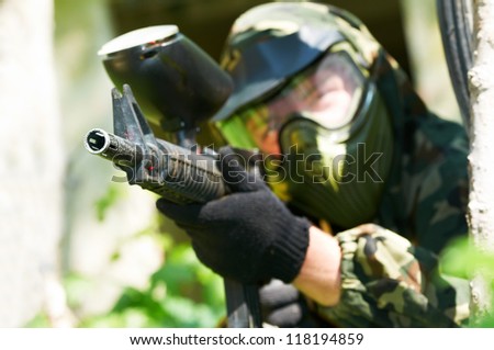 paintball sport player in protective uniform and mask aiming and shooting with gun outdoors. Shallow DOF