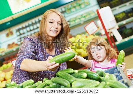 woman and little girl choosing cucumbers during shopping at fruit vegetable supermarket