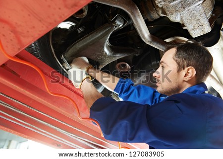 car mechanic tighten screw in make suspension adjustment with spanner during automobile wheel alignment work at repair service station