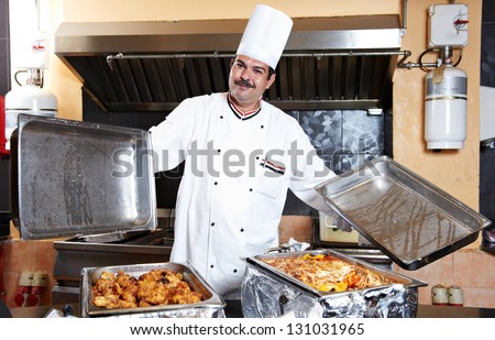 Adult arab chef man in uniform demonstrating food on cooker in resort hotel restaurant kitchen