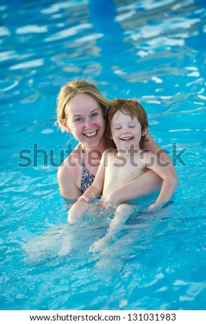 Happy smiling woman and child playing at water park in resort hotel swimming pool