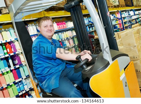 young smiling warehouse worker driver in uniform in forklift stacker loader in supermarket