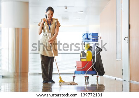 Adult cleaner maid woman with mop and uniform cleaning corridor pass or hall floor of business building