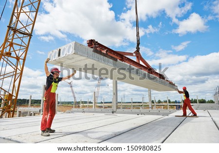 workers in safety protective equipment installing concrete floor slab panel at building construction site
