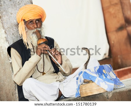 Hindu Snake charmer adult man in turban playing on musical instrument before snake at a basket