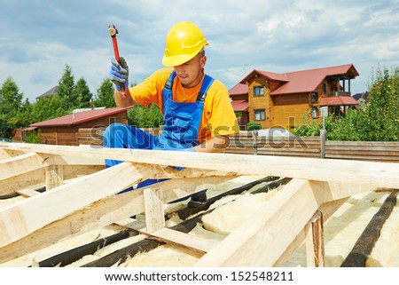roofer carpenter worker nailing wood board with hammer on roof installation work