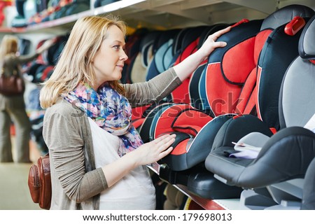 woman choosing child car seat for newborn baby in shop supermarket