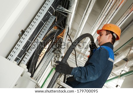electrician builder engineer installing industrial cable into fuse box