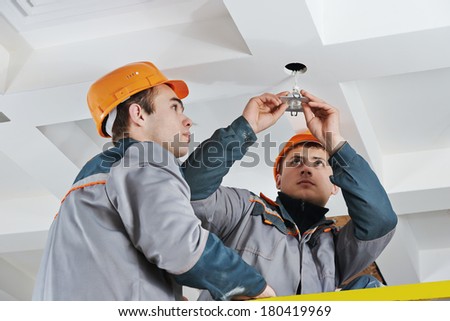 electrician worker in uniform installing or replacing spot light lamp into ceiling