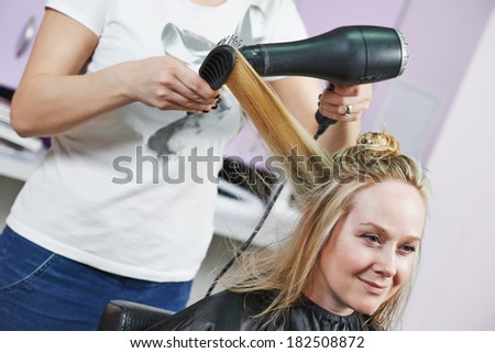 hairdresser drying hair with blow dryer of woman client at beauty parlour after highlighting