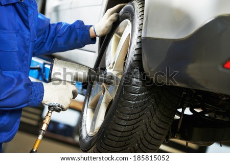 car mechanic screwing or unscrewing car wheel of lifted automobile by pneumatic wrench at repair service station