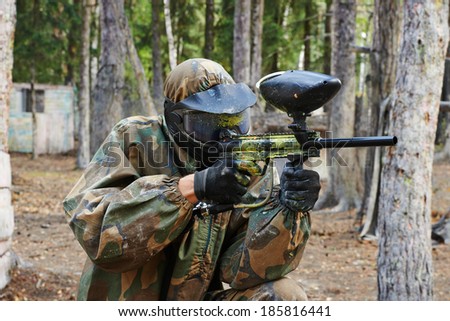paintball sport player man in protective camouflage uniform and mask with marker gun outdoors