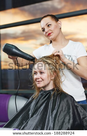 Female hairdresser drying hair with blow dryer of woman client at beauty parlour after highlighting