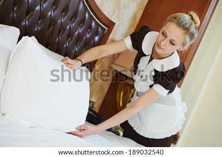 Hotel service. female housekeeping worker maid making bed with bedclothes at inn room