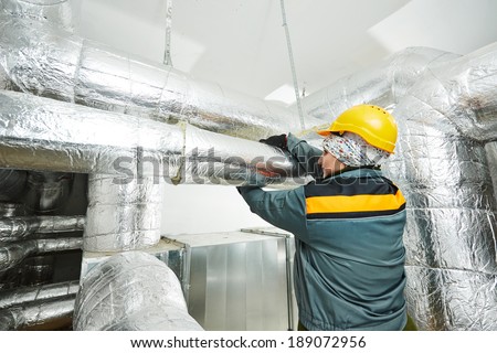 Thermal insulation. Female insulation worker isolating industrial pipe with glass wool and foil