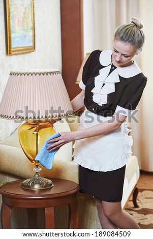 Hotel service. female housekeeping worker with cleaning table from dust in room