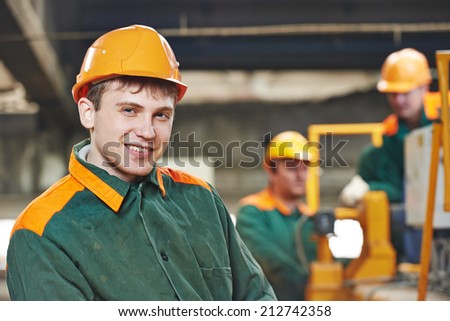Happy young adult electrician builder engineer in front of his co-worker screwing equipment in fuseboard